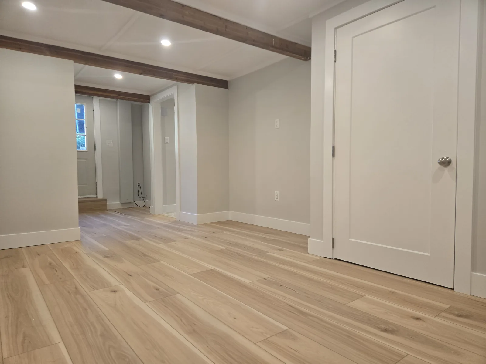 Finished basement living space with wood beams, recessed lights and wood-look flooring
