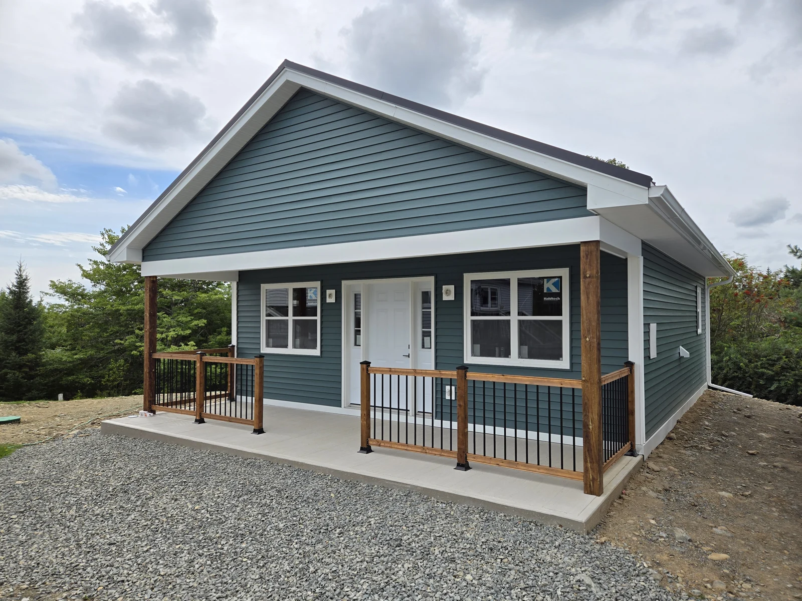 Blue-sided home with a covered porch and timber railings, with site finishing underway